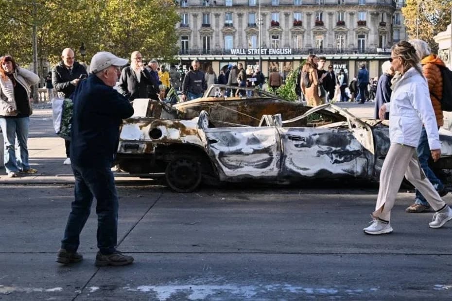 Gente mira a un auto calcinado en Place de la Republique el día después de una manifestación contra el creciente coste de la vida, que se suma a las protestas estudiantiles, en París, el domingo 18 de octubre de 2026.