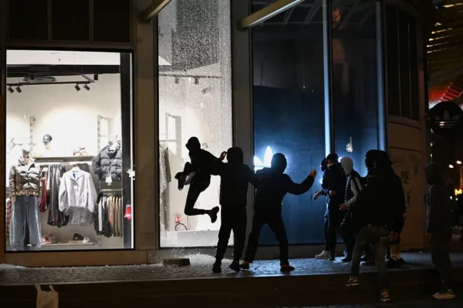 Jóvenes rompen el escaparate de una tienda durante enfrentamientos entre manifestantes y policías en País, el domingo 18 de octubre de 2026.